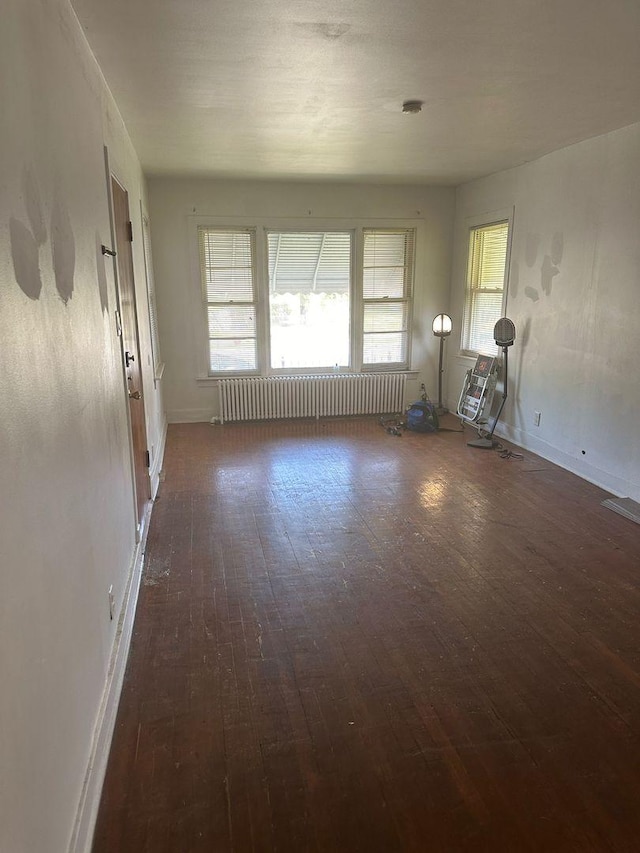 empty room featuring radiator heating unit, visible vents, baseboards, and hardwood / wood-style floors