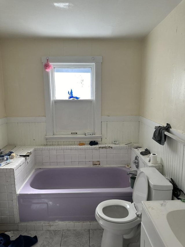 full bath featuring toilet, a wainscoted wall, a bathing tub, and tile patterned floors