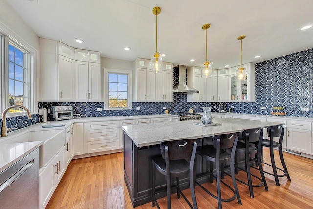 kitchen featuring wall chimney exhaust hood, stainless steel appliances, pendant lighting, a center island, and white cabinetry