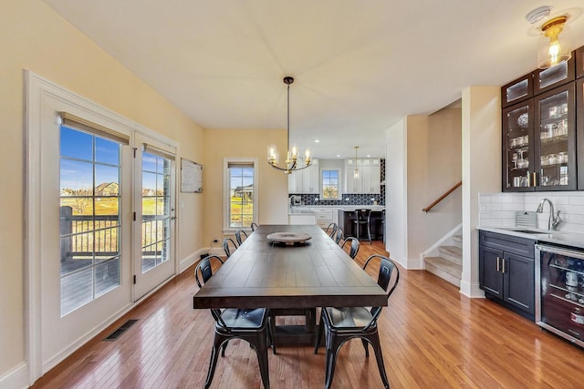 dining area featuring wine cooler, sink, a chandelier, and light wood-type flooring