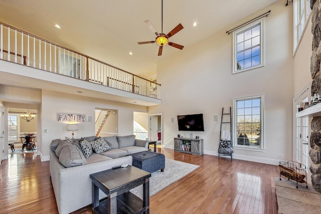 living room featuring hardwood / wood-style floors, ceiling fan with notable chandelier, a towering ceiling, and a fireplace