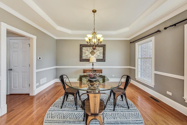 dining area featuring hardwood / wood-style floors, a raised ceiling, and crown molding