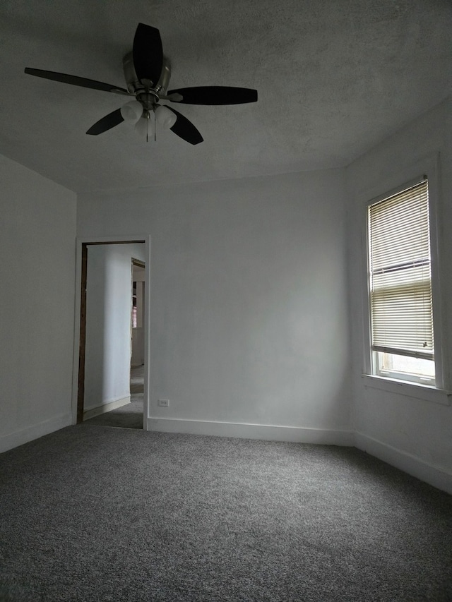 spare room with a textured ceiling, dark colored carpet, and ceiling fan