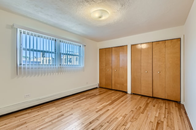 unfurnished bedroom with light hardwood / wood-style flooring, two closets, a baseboard heating unit, and a textured ceiling