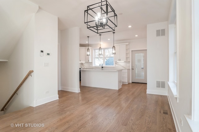 interior space with decorative light fixtures, white cabinets, an inviting chandelier, sink, and light hardwood / wood-style floors