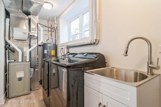 clothes washing area with heating utilities, washer and clothes dryer, sink, water heater, and light hardwood / wood-style flooring