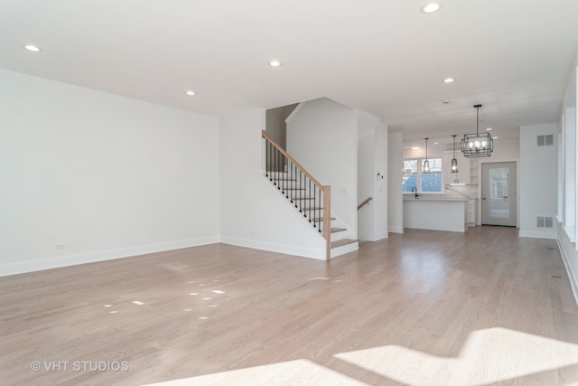 unfurnished living room featuring a notable chandelier, light hardwood / wood-style floors, and sink