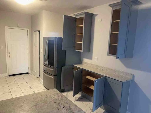 kitchen featuring blue cabinetry, stainless steel refrigerator, light tile floors, and light stone counters