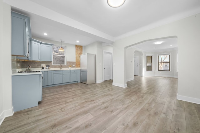 kitchen featuring hanging light fixtures, backsplash, sink, light hardwood / wood-style flooring, and crown molding