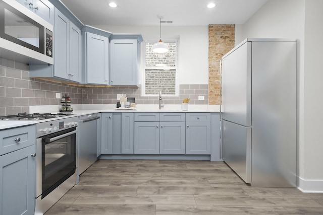 kitchen featuring pendant lighting, backsplash, light hardwood / wood-style flooring, and stainless steel appliances