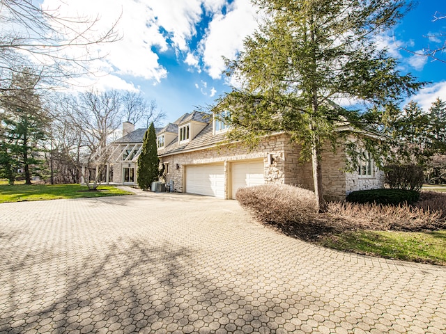 view of front facade with stone siding, an attached garage, and decorative driveway