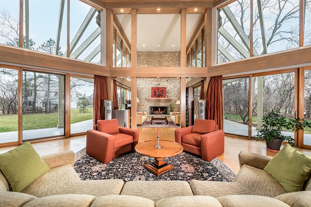 living room featuring a wealth of natural light, light wood-type flooring, a stone fireplace, and a towering ceiling