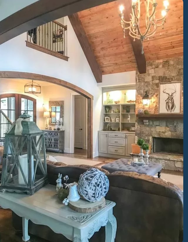 interior space with high vaulted ceiling, built in features, a chandelier, wood ceiling, and a stone fireplace