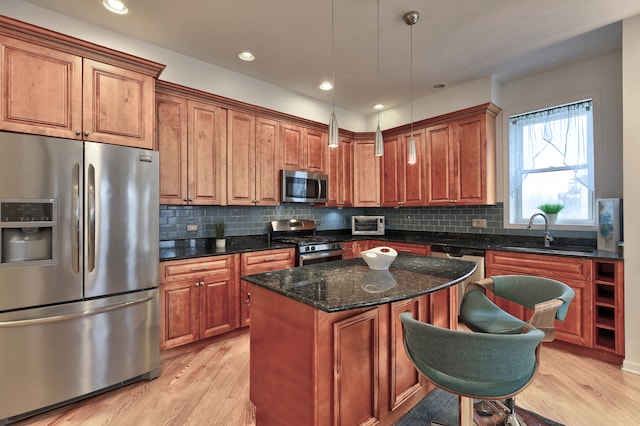 kitchen featuring stainless steel appliances, decorative light fixtures, a kitchen island, light hardwood / wood-style flooring, and sink