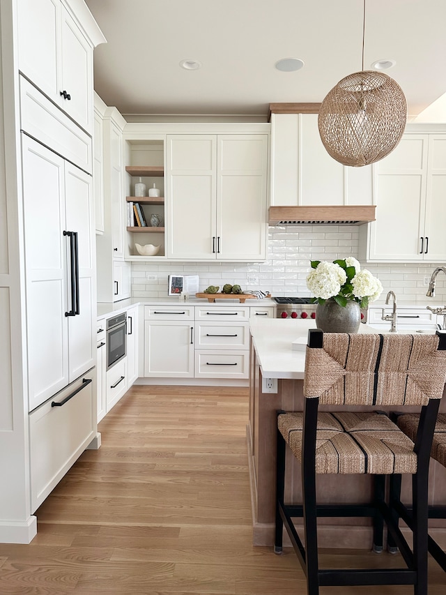 kitchen with a breakfast bar area, light hardwood / wood-style flooring, tasteful backsplash, and white cabinetry