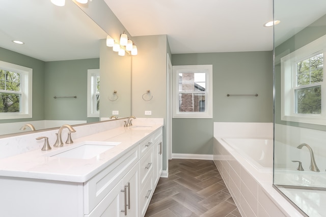 bathroom with a wealth of natural light, a relaxing tiled bath, and dual vanity