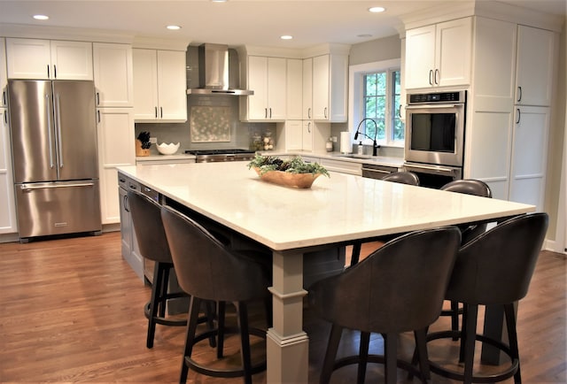 kitchen featuring wall chimney exhaust hood, light hardwood / wood-style flooring, stainless steel appliances, and a kitchen bar