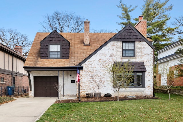 tudor-style house with brick siding, a chimney, an attached garage, driveway, and a front lawn