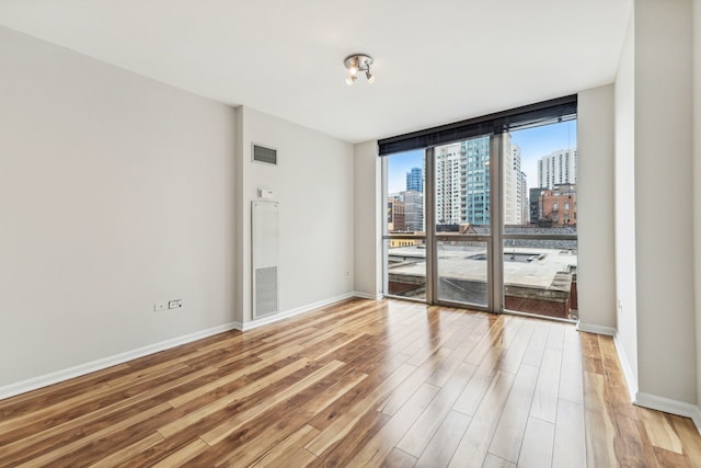 spare room featuring a wall of windows and light wood-type flooring