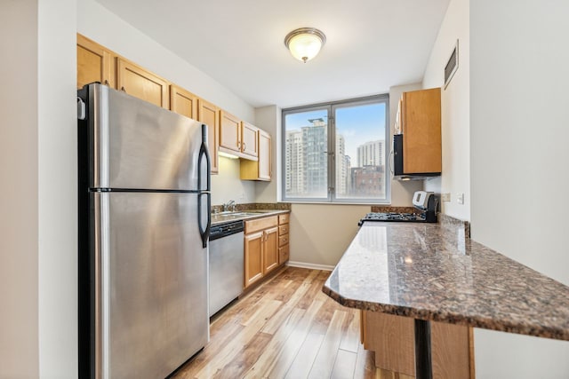 kitchen with dark stone counters, appliances with stainless steel finishes, light hardwood / wood-style floors, kitchen peninsula, and sink