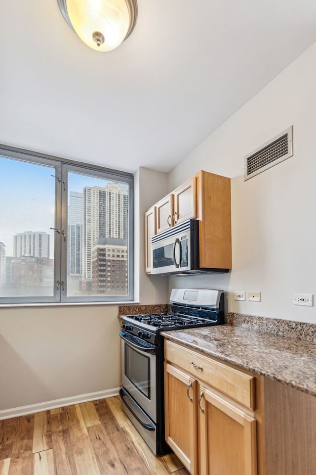 kitchen featuring appliances with stainless steel finishes, dark stone counters, and light hardwood / wood-style floors