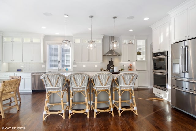 kitchen with wall chimney range hood, stainless steel appliances, decorative light fixtures, dark hardwood / wood-style floors, and white cabinets