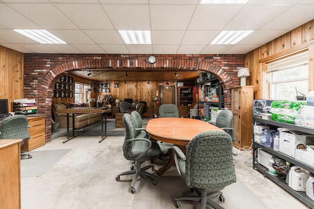 office space featuring concrete flooring, wood walls, arched walkways, and a paneled ceiling