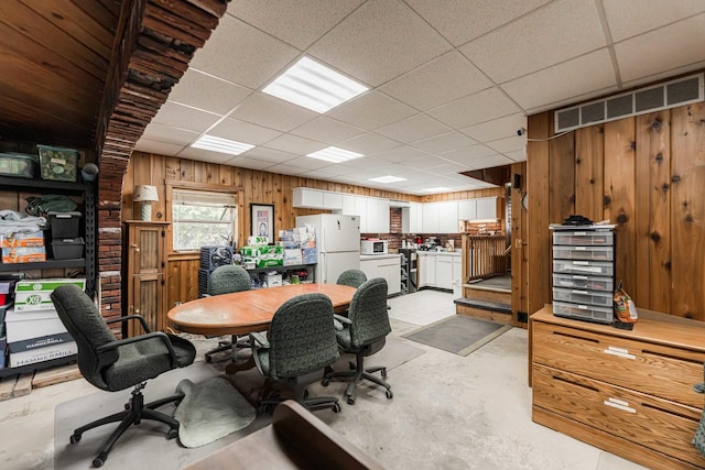 office space featuring concrete floors, a paneled ceiling, and wooden walls