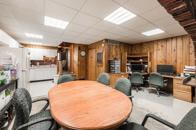 office with a sink, wood walls, visible vents, and a drop ceiling