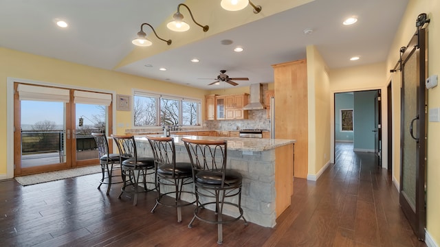 kitchen featuring a barn door, tasteful backsplash, wall chimney range hood, and dark hardwood / wood-style flooring