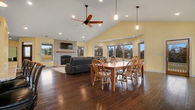 dining area with ceiling fan, a stone fireplace, dark wood-type flooring, and high vaulted ceiling