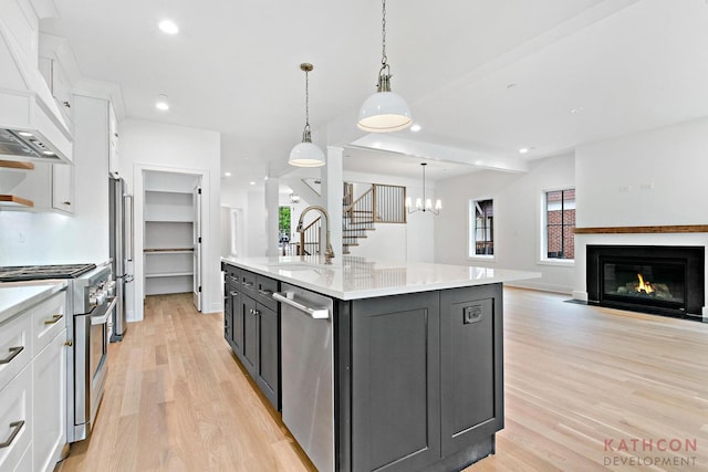 kitchen with premium range hood, hanging light fixtures, white cabinets, a center island with sink, and light hardwood / wood-style floors