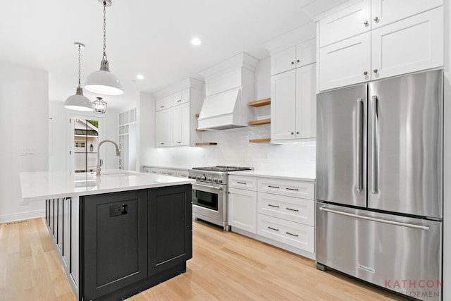 kitchen featuring decorative light fixtures, a center island with sink, light wood-type flooring, and stainless steel appliances