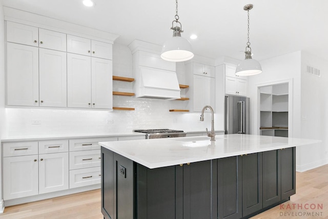 kitchen featuring light hardwood / wood-style flooring, high quality fridge, hanging light fixtures, and an island with sink