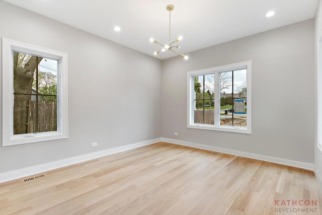 spare room with a healthy amount of sunlight, light hardwood / wood-style flooring, and a notable chandelier