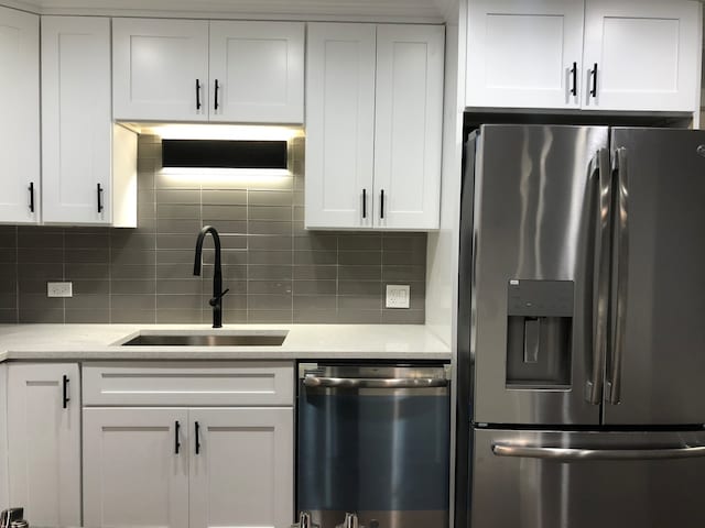 kitchen featuring stainless steel appliances, light stone countertops, tasteful backsplash, white cabinetry, and sink