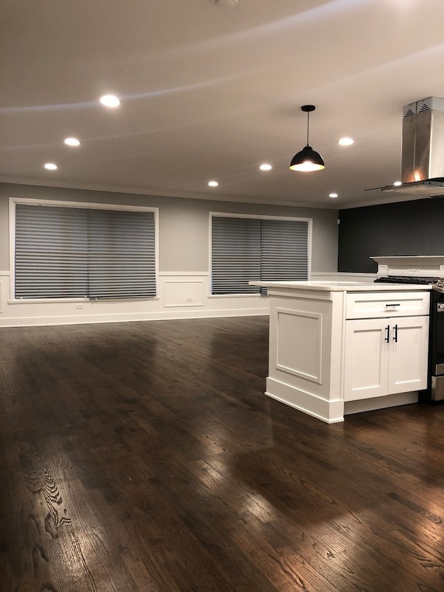 kitchen featuring gas range oven, white cabinets, dark wood-type flooring, wall chimney range hood, and decorative light fixtures