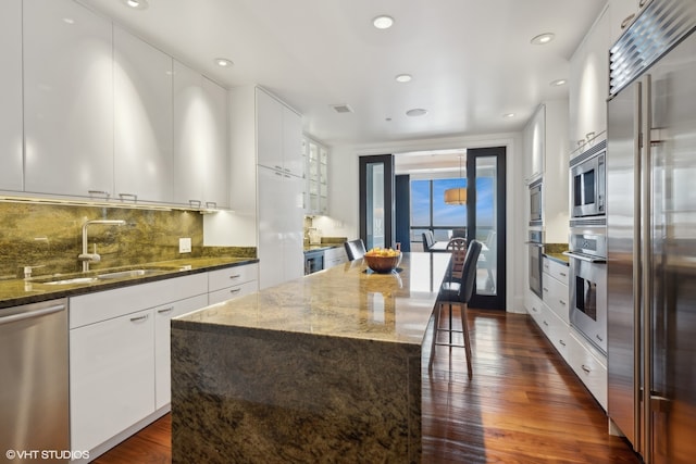 kitchen with tasteful backsplash, a center island, built in appliances, dark hardwood / wood-style floors, and white cabinets