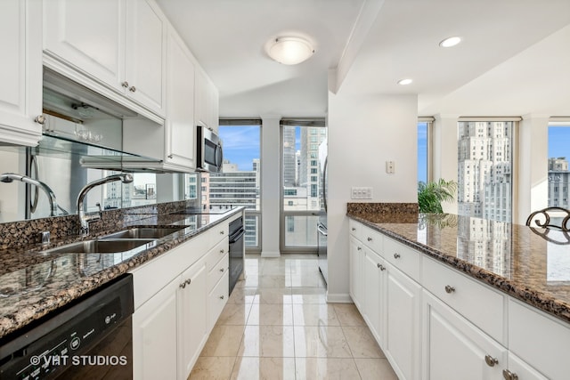 kitchen with light tile flooring, dark stone countertops, dishwasher, sink, and white cabinetry