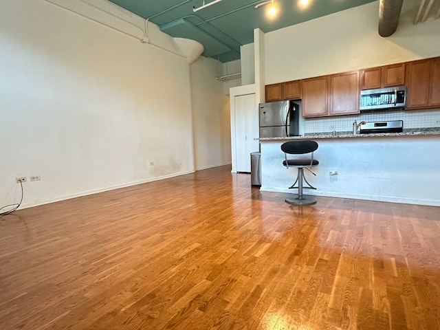 kitchen with a towering ceiling, a kitchen breakfast bar, appliances with stainless steel finishes, and light wood-type flooring