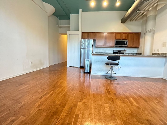 kitchen with tasteful backsplash, wood-type flooring, appliances with stainless steel finishes, and a high ceiling