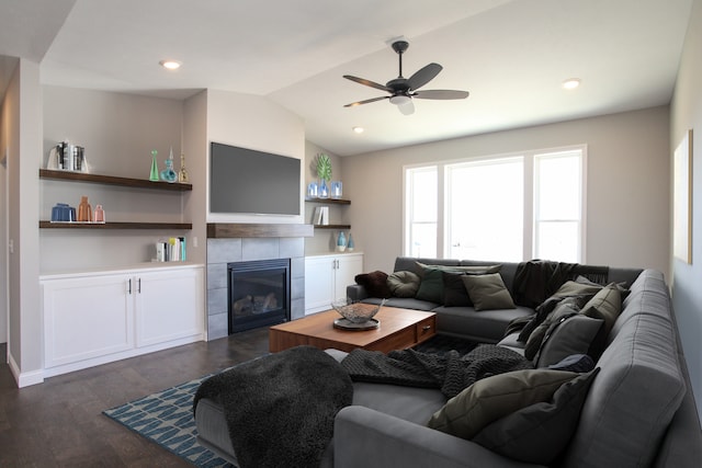 living room with ceiling fan, built in shelves, dark wood-type flooring, a tiled fireplace, and vaulted ceiling