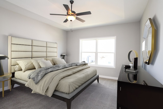 bedroom with ceiling fan, dark carpet, and a raised ceiling