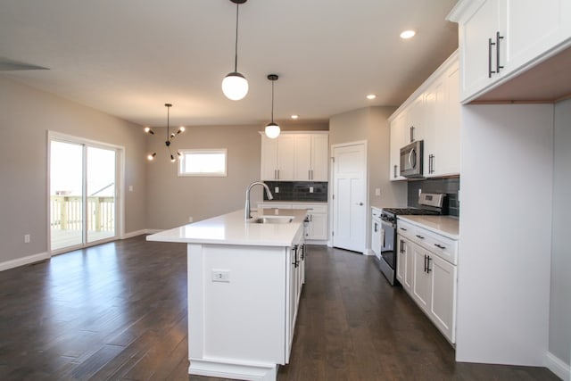 kitchen featuring white cabinets, tasteful backsplash, decorative light fixtures, stainless steel appliances, and a center island with sink