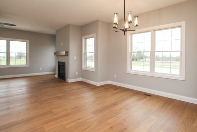 unfurnished living room with a healthy amount of sunlight, light wood-type flooring, and an inviting chandelier