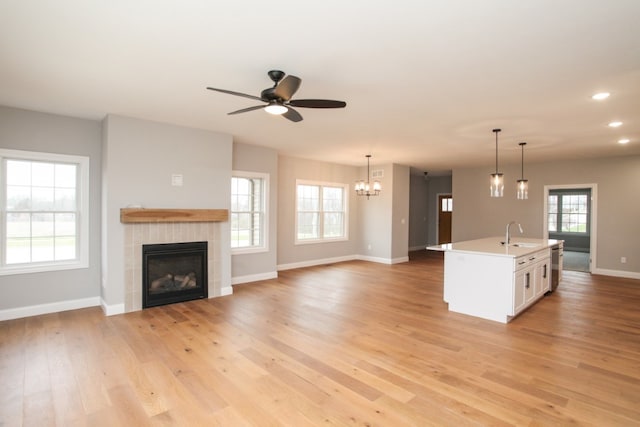 unfurnished living room featuring a tiled fireplace, ceiling fan with notable chandelier, a wealth of natural light, and light wood-type flooring