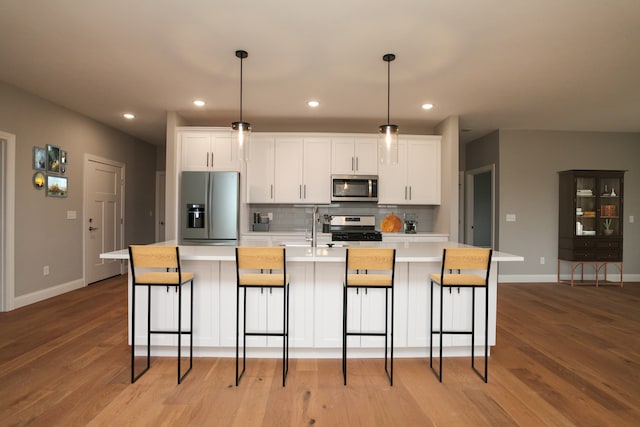 kitchen with stainless steel appliances, white cabinetry, light hardwood / wood-style floors, and an island with sink