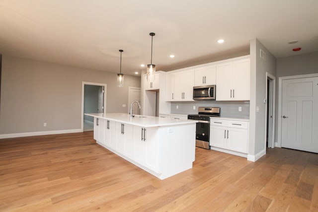 kitchen with stainless steel appliances, white cabinetry, a kitchen island with sink, light wood-type flooring, and sink