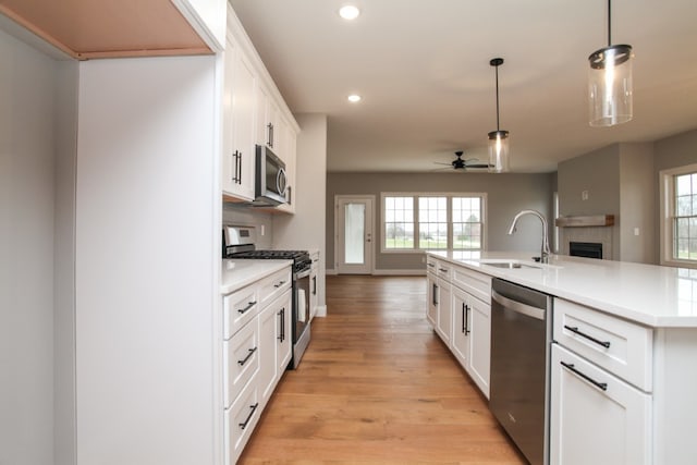 kitchen with ceiling fan, white cabinets, appliances with stainless steel finishes, light hardwood / wood-style floors, and a center island with sink