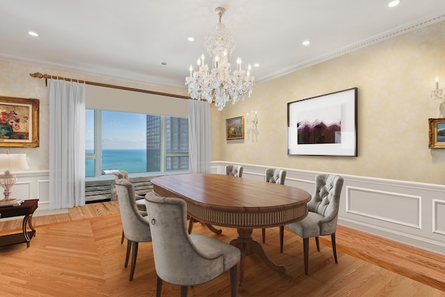 dining area with a water view, light wood-type flooring, crown molding, and an inviting chandelier